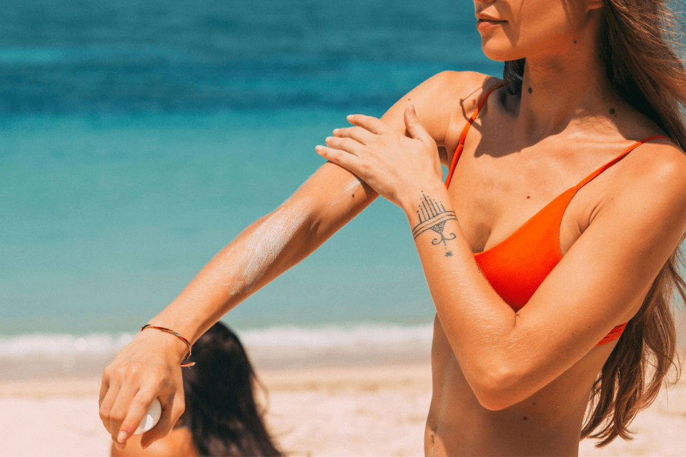A young woman on the beach applies the best non-toxic sunscreen to stay protected under the sun and enjoy her summer to the maximum potential